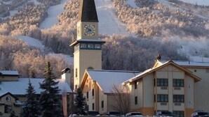 A building with a clock tower, surrounded by snow-covered trees and a ski slope in the background. - ⛷️Slope side Condo- (Stratton)