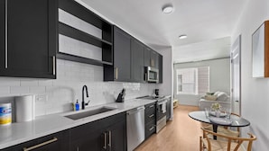A modern kitchen with dark cabinets, a white countertop, and a dining area with a round table and chairs. - The Perfect Studio | 1 Queen Bed | Raymond James! (Tampa)