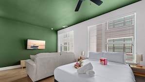 A bedroom with a bed, two sofas, a painting, and large windows with blinds. - The Perfect Studio | 1 Queen Bed | Raymond James! (Tampa)