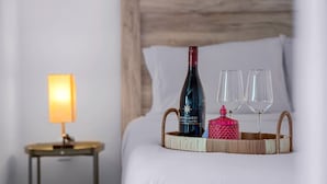 Un lit bien fait, agrémenté d’une bouteille de vin rosé, de deux verres et d’un joli récipient décoratif posé sur un plateau en osier.
