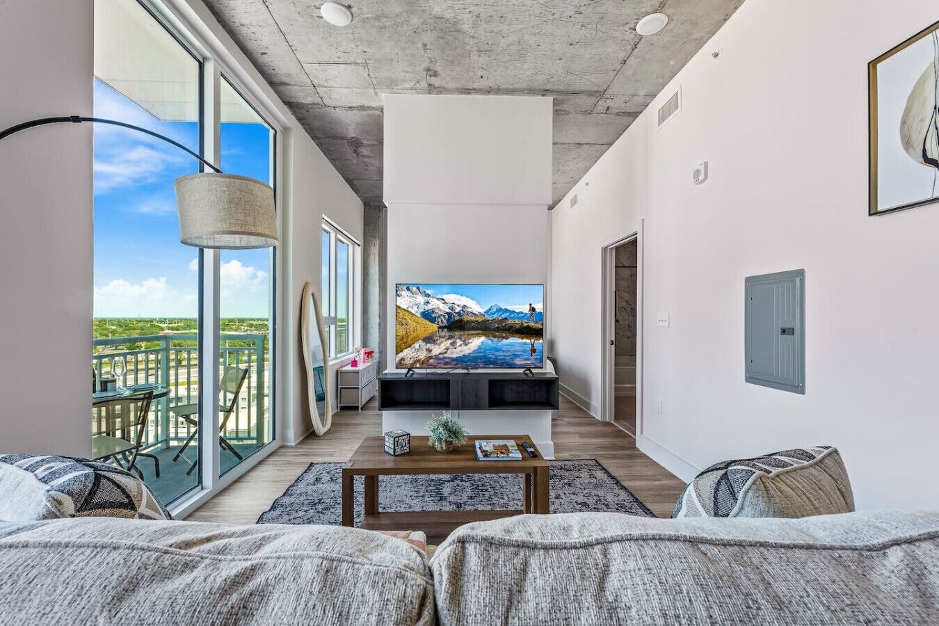 Een moderne woonkamer met een grote televisie, een balkon met buitenmeubels en uitzicht op de bergen.