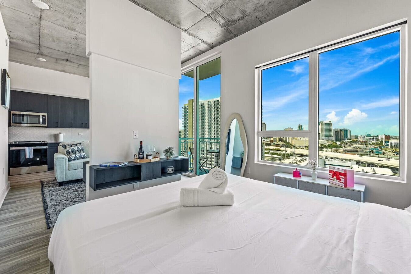 Een moderne hotelkamer met een groot bed, een zithoek met een bank en een tafeltje, een ingebouwde televisie en een groot raam met uitzicht op de stad.