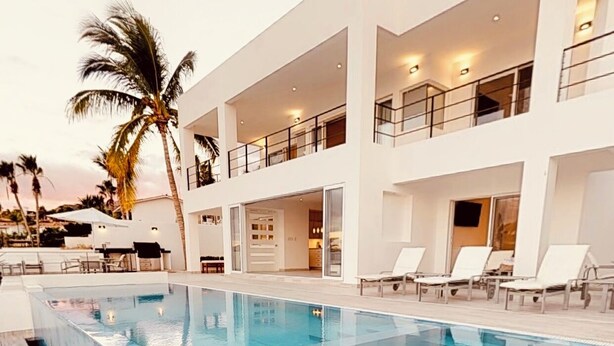 A modern hotel with a large pool, multiple balconies, and palm trees.