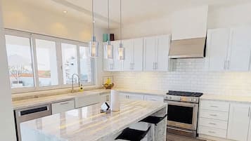Une cuisine moderne dotée d’un grand îlot central, de tabourets de bar, d’appareils électroménagers en acier inoxydable et de meubles de rangement blancs.