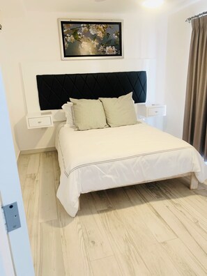 A neatly arranged bedroom with a bed, a headboard, a bedside table, and a wall-mounted painting.