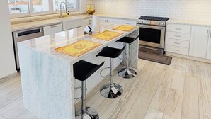 A modern kitchen with a central island, bar stools, a stove, and a large window.