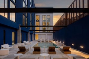 A rooftop pool area with lounge chairs and tables, surrounded by blue walls and a modern building.