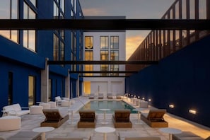A rooftop pool area with lounge chairs and tables, surrounded by blue and white buildings.