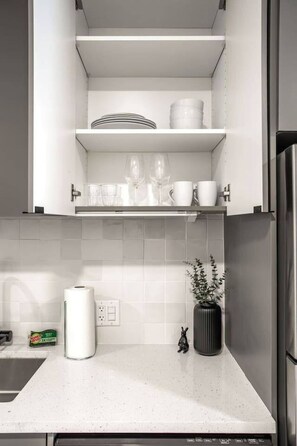 Eine Küche mit weißen Schränken, einer Arbeitsplatte, einem Spülbecken, einer Küchenpapierrolle, einem kleinen Topfpflanzen und einem Toaster.