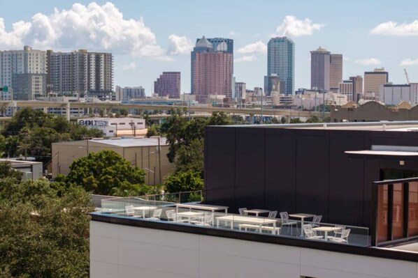 Eine Stadtansicht mit Hochhäusern, einer Dachterrasse mit Tischen und Stühlen und einem Gebäude mit der Aufschrift 'BOLTS'.