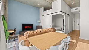 Una sala moderna con una mesa de comedor de madera, un sofá y un televisor mostrando 'NETFLIX'.