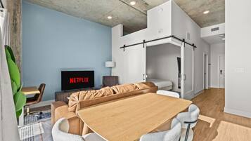 A modern living room with a wooden dining table, a sofa, and a TV displaying 'NETFLIX'.
