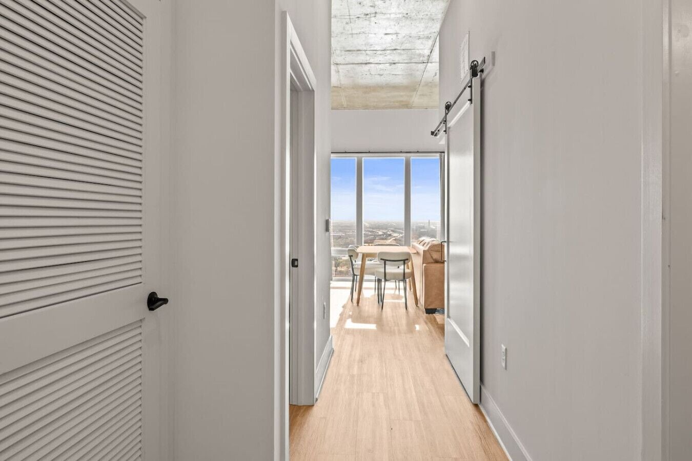 A narrow hallway with a wooden floor leading to a balcony with a table and chairs.
