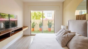 A modern hotel room with a large bed, a TV on a wooden console, a balcony with potted plants, and a large mirror on the wall.