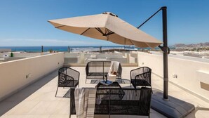 A rooftop terrace with outdoor seating, a large umbrella, and a view of the sea.