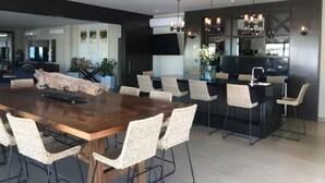 A modern kitchen with a large island, dining area with a wooden table and wicker chairs, and a visible kitchen counter with a sink and stove.