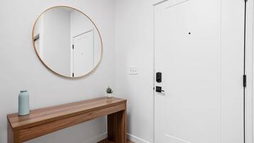 A hallway with a wooden bench, a round mirror, a white door, and a small potted plant.