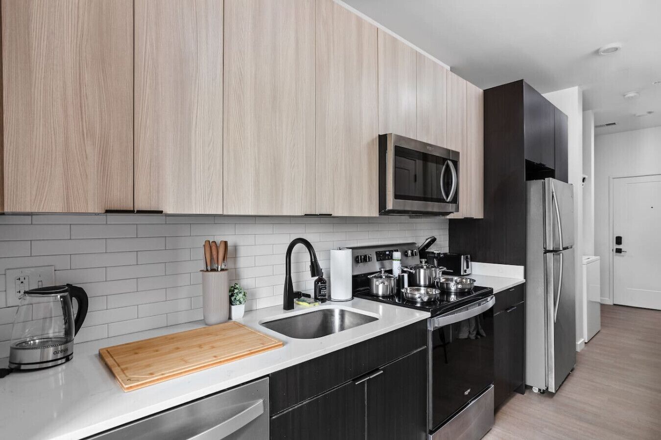 Une cuisine moderne avec des meubles de couleur bois clair, un réfrigérateur en acier inoxydable, un four à micro-ondes et une cuisinière.