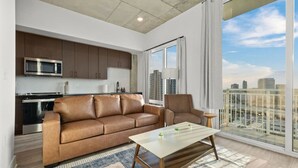 A modern living room with a leather sofa, a glass coffee table, and a view of a cityscape through large windows.
