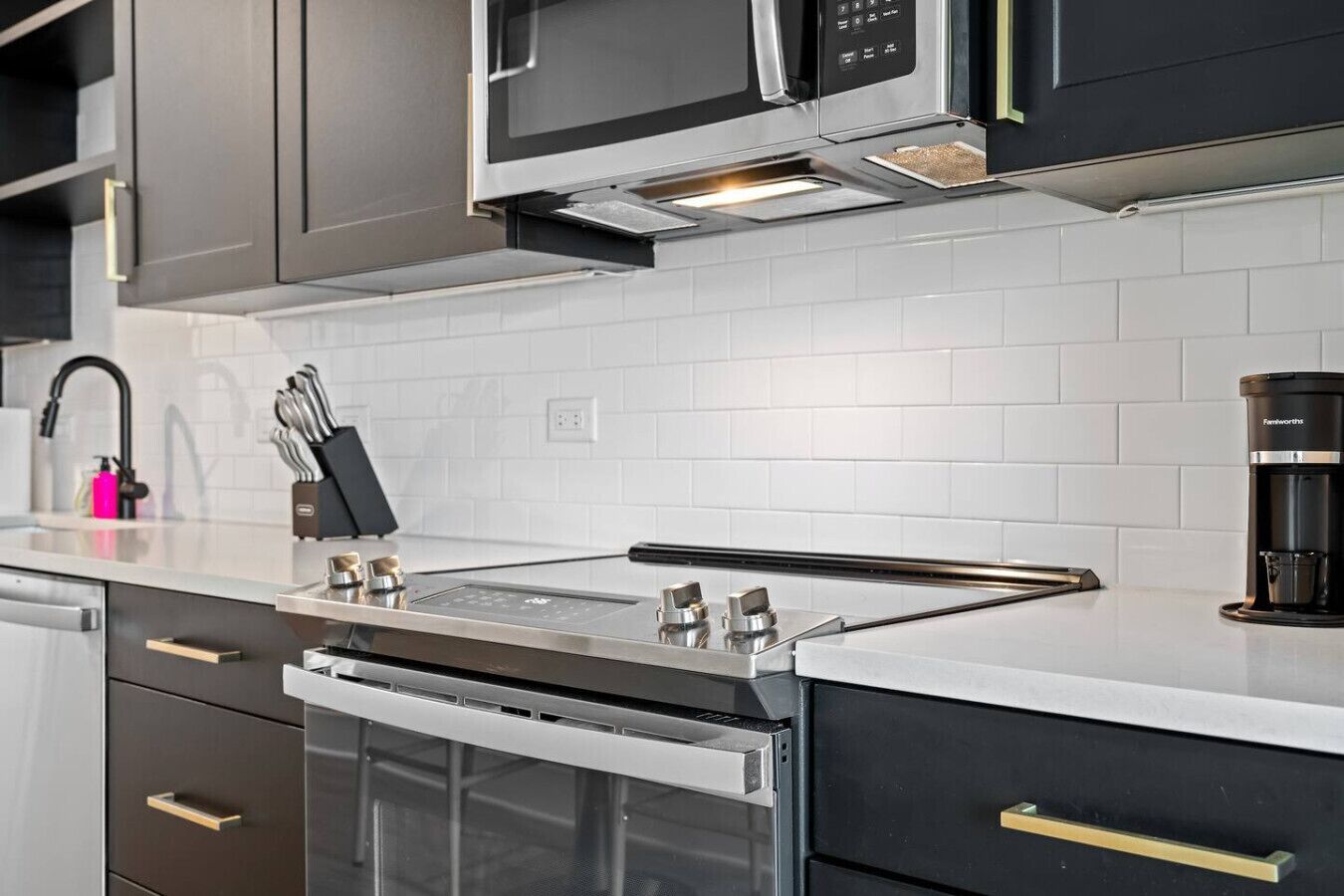A modern kitchen with stainless steel appliances, a white tiled backsplash, and dark cabinetry.