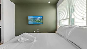 Habitación de hotel con cama, televisor de pantalla plana en la pared y ventana con persianas.