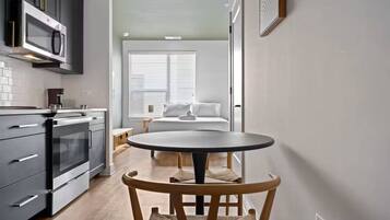 Una cocina compacta con electrodomésticos modernos, un comedor con una mesa redonda y una silla de madera, y un dormitorio con cama y ventana.