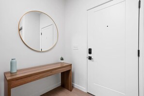 A hallway with a wooden bench, a round mirror, a white door, and a small potted plant.