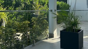 Un balcone moderno all'aperto con ringhiera in vetro, immerso nel verde e con cielo azzurro.
