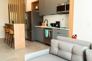Una cocina moderna con electrodomésticos de acero inoxidable, una zona de bar con taburetes y un sofá gris en la sala de estar.