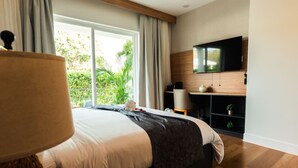 Una camera da letto moderna con un letto grande, una TV fissata al muro e vista su del verde all'esterno.