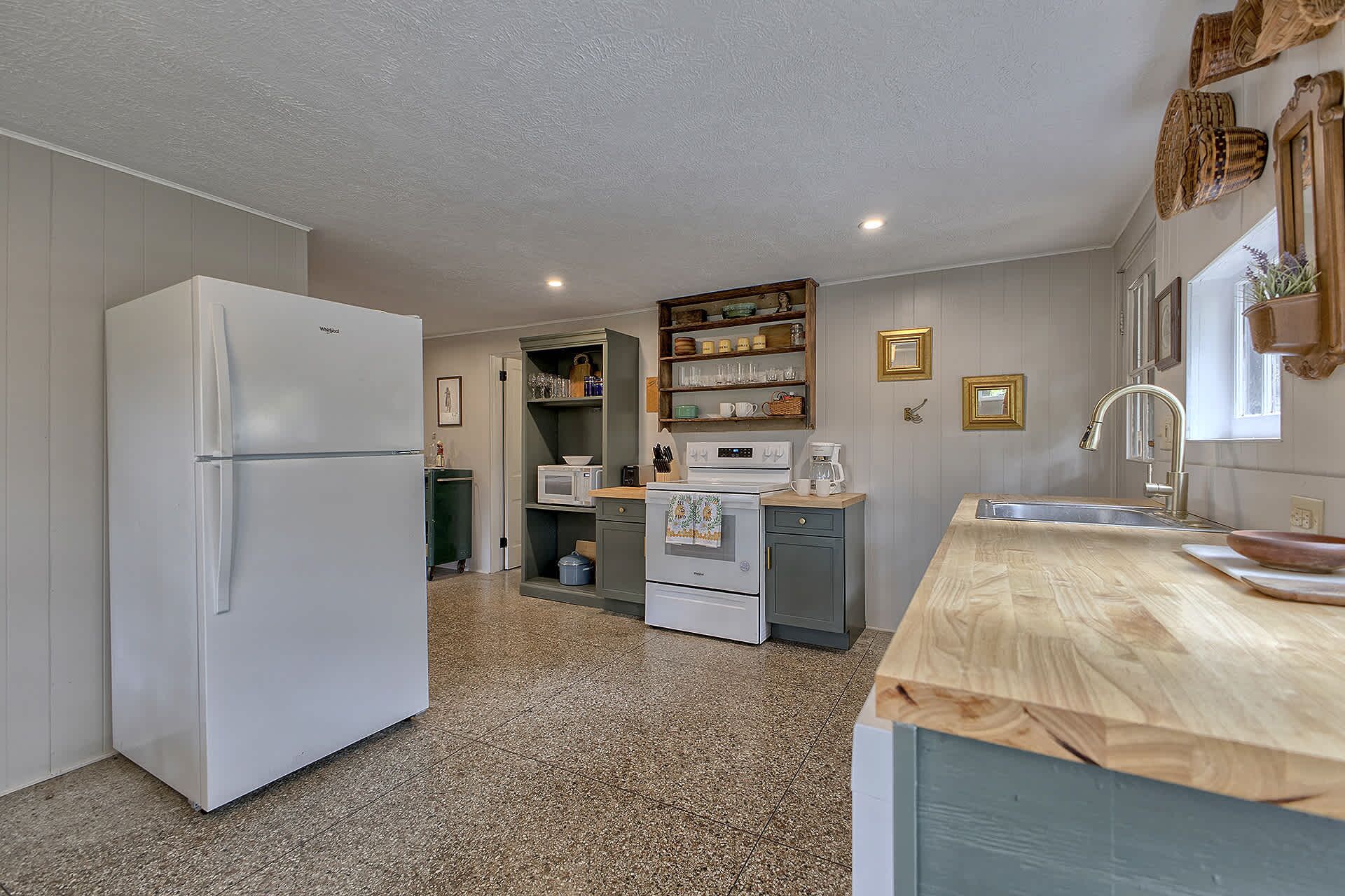 A compact kitchen with a refrigerator, microwave, oven, and wooden countertop.