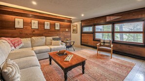 Una sala de estar acogedora con un sofá modular, una mesa de centro de madera y un ventanal con vistas a árboles.