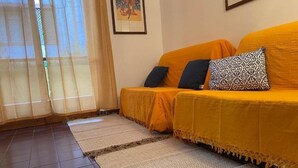 A room with a sofa set, a patterned cushion, and a window with sheer curtains.