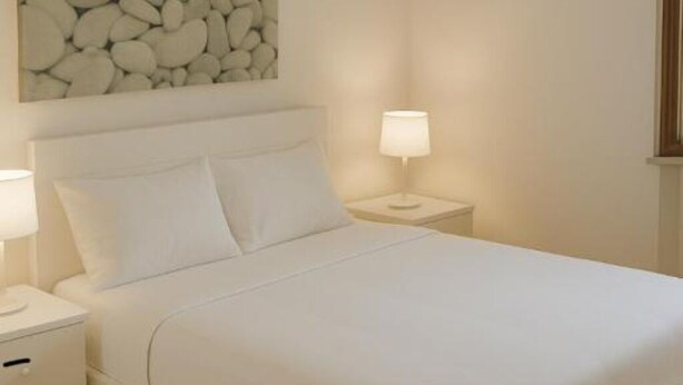 A neatly made bed with white linens, a headboard, and two bedside lamps.