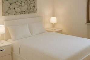 A neatly made bed with white linens, a headboard, and two bedside lamps.