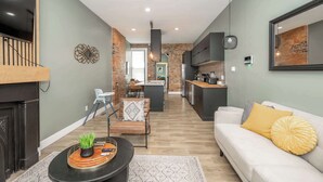 Uma sala de estar moderna com sofá, mesa de centro e televisão. Cozinha visível ao fundo, com área de jantar.