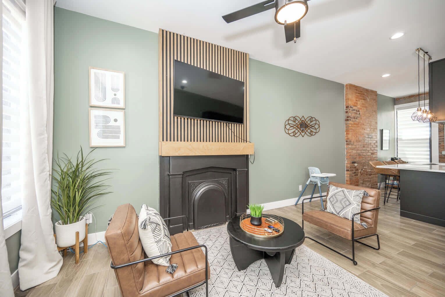 A modern living room with a fireplace, leather sofas, a coffee table, and a dining area with a kitchen in the background.