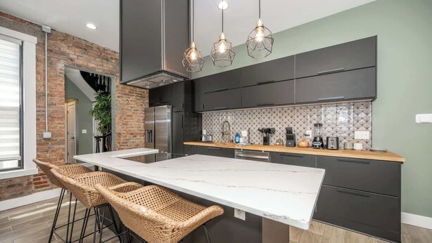 Cozinha moderna com uma ilha grande, armários escuros e backsplash de ladrilho em padrão herringbone.