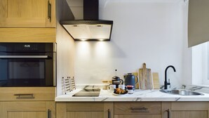 Una cocina moderna con armarios de madera, horno empotrado, pileta de acero inoxidable y cafetera.