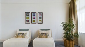 Una habitación con dos sillones blancos, una planta grande en maceta y tres cuadros en la pared.