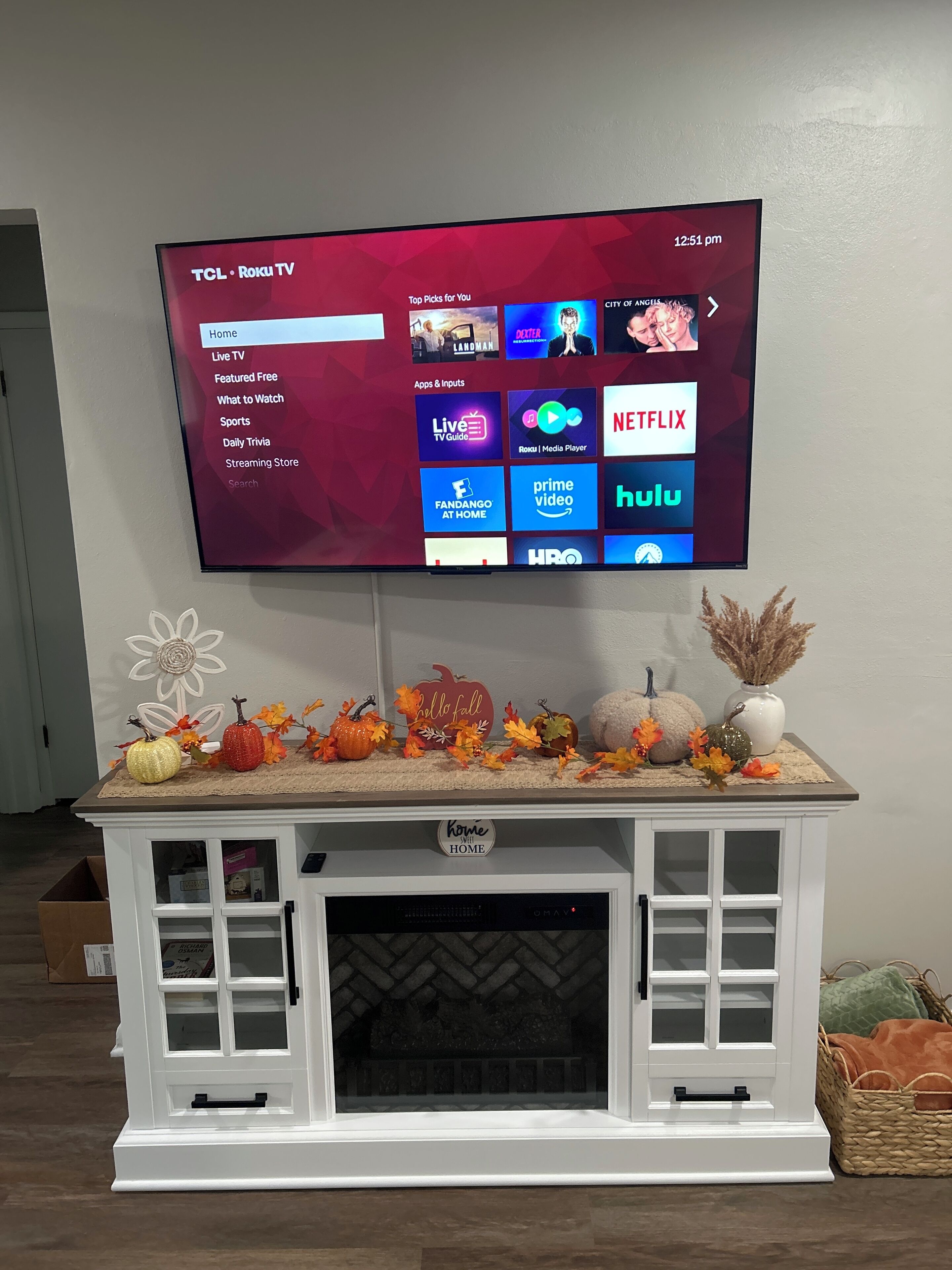 A TCL Roku TV mounted on a wall above a white entertainment center with a fireplace below.