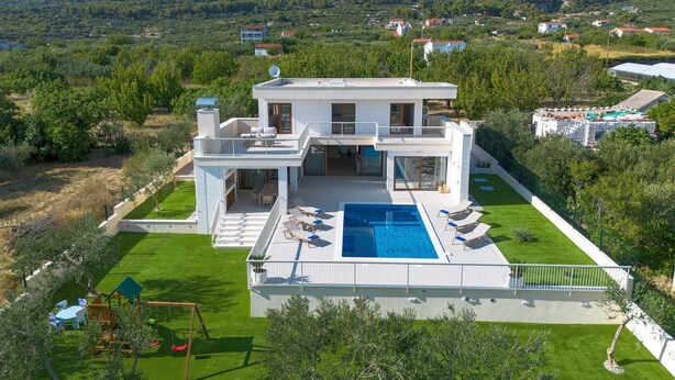 A modern two-story house with a large swimming pool, surrounded by lush greenery and a mountainous backdrop. - Villa Mood – Pool, Gym & Sauna near Split (Kastel Luksic)