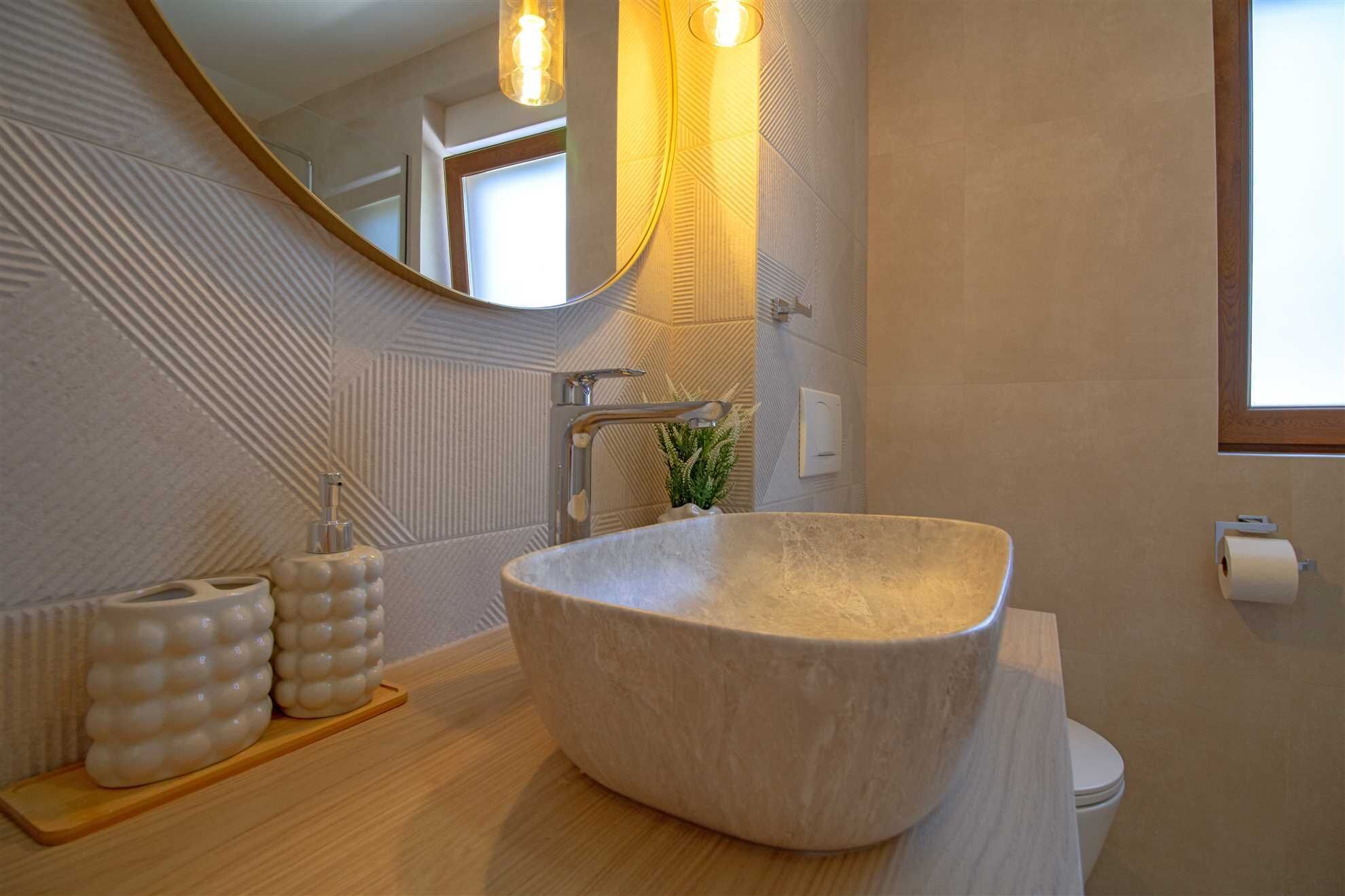 Un bagno moderno con un ampio lavabo di pietra a forma ovale, un mobile contenitore in legno, uno specchio e un water.