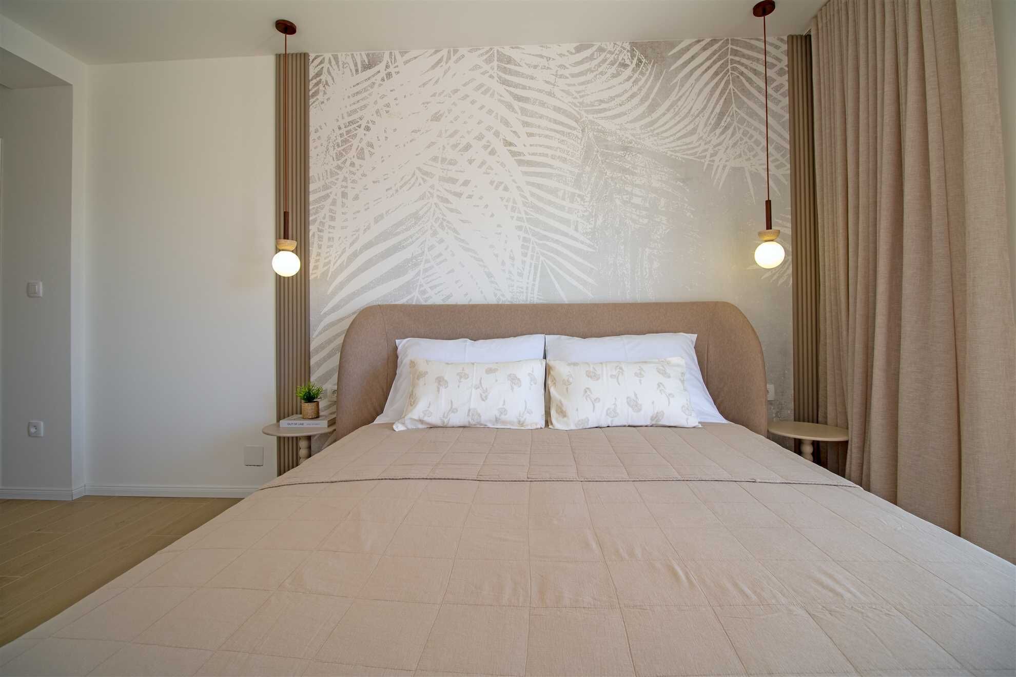 A bedroom with a large bed, two bedside tables, a wall with a leaf pattern, and a curtain.