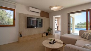 A modern living room with a flat-screen TV, a round coffee table, a sofa, and a balcony with a pool view. - Villa Mood – Pool, Gym & Sauna near Split (Kastel Luksic)
