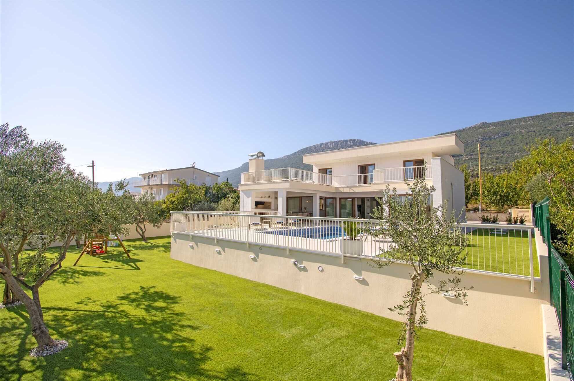 A modern two-story house with a swimming pool, surrounded by well-maintained lawns and trees.