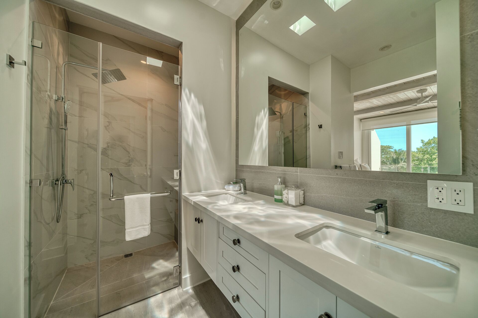 Un baño moderno con ducha envuelta en vidrio, un espejo grande y un tocador blanco con cajones.