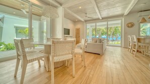 Un vaste espace de vie doté d’un plancher en bois, d’un canapé et de chaises blanches. De grandes fenêtres offrent une vue sur l’extérieur.