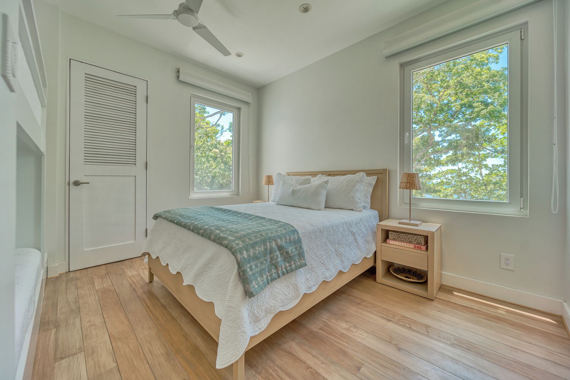 A bedroom with a bed, a nightstand, a ceiling fan, and two windows.