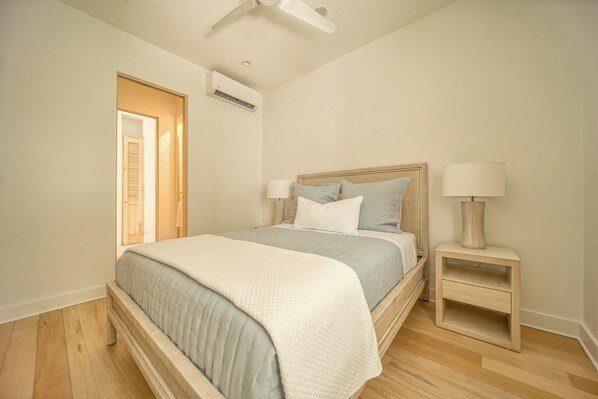 A bedroom with a bed, bedside lamps, a nightstand, and an air conditioning unit. - Watercolors Roatan (Roatán)